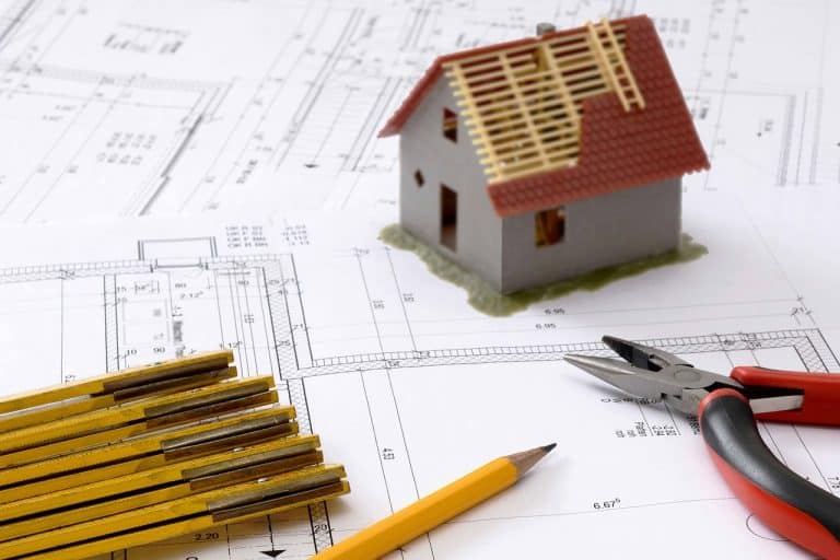 Ein Hausmodell und Bleistifte auf Bauplänen, die Ingenieurleistungen zeigen.