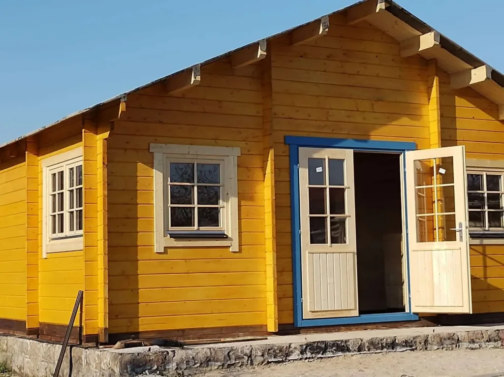 Gelb gestrichenes Holzhaus mit blauer Tür und weißen Fenstern